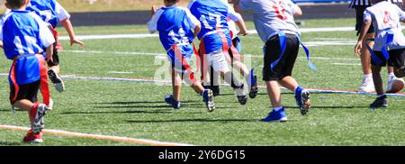 Young boys chasing each other playing youth flag football on a turf field. Stock Photo