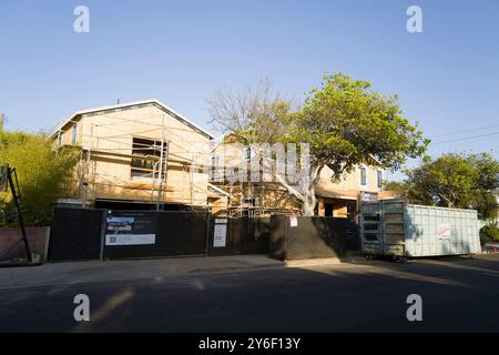 New homes under construction with scaffolding and plywood walls. Workers on-site, building in progress, surrounded by trees and construction equipment Stock Photo