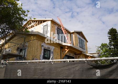 New homes under construction with scaffolding and plywood walls. Workers on-site, building in progress, surrounded by trees and construction equipment Stock Photo