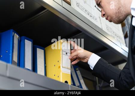 Close up of businessman's hand picking up yellow folder from shelf in office Stock Photo