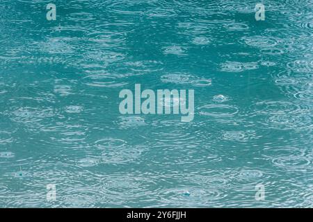 raindrops falling on a swimming pool, raindrops falling on water creating patterns, interesting patterns formed on water's surface creating patterns. Stock Photo