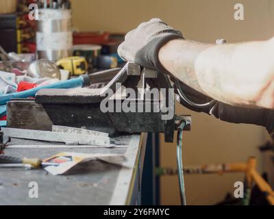 Bicycle mechanic wearing gloves is using a bench vise to hold a piece of metal while he works on a bicycle frame in his repair shop Stock Photo