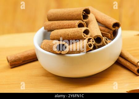Cinnamomum verum, cinnamon sticks in a white bowl on a wooden background Stock Photo