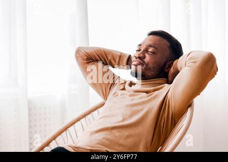 Black Guy Relaxing Sitting On Modern Chair Against Window Indoor Stock Photo
