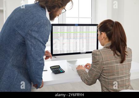 Male accountant helping a female colleague with business sheets on a desktop computer Stock Photo