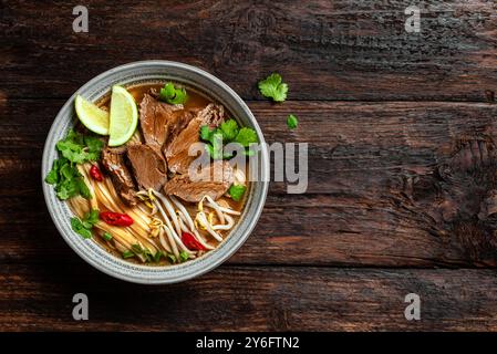 Pho Bo Vietnamese soup, bowl of fresh asian soup with rice noodle, beef meat, herbs, soy sprouts and chili on wooden background, copy space. Homemade Stock Photo