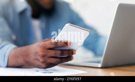 Unrecognizable black entrepreneur using smartphone and working on laptop Stock Photo