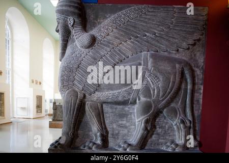 A massive Assyrian winged lion figure with a human head stands in the Pergamon Museum, attracting visitors in Berlin, Germany. Stock Photo