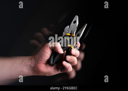 Close up of man's hand holding three different cable cutting pliers with motion effect against black background Stock Photo