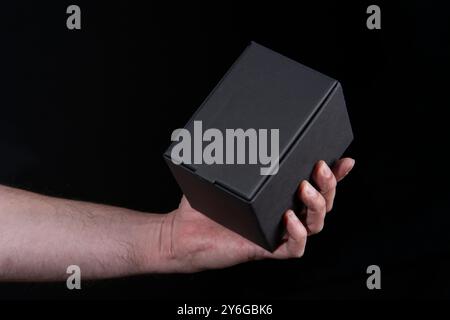 Close up of man's hand holding a small black cardboard box against black background Stock Photo