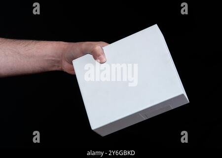 Close-up of man's hand holding a large white cardboard box against black background Stock Photo