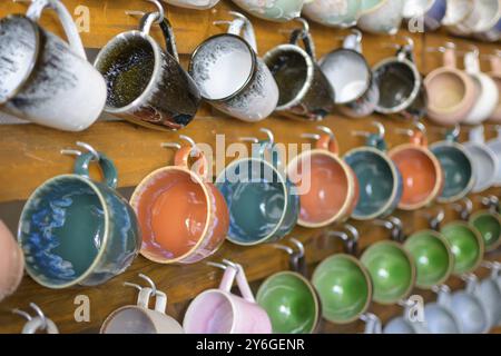 Collection of colorful ceramic mugs hanging on a wooden wall Stock Photo