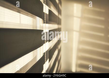 Sun shining through window roller blinds throwing shadows on the wall. Atmospheric mood. Selective focus Stock Photo