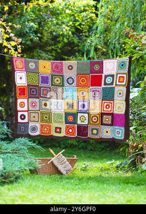 Handmade vintage crochet granny square hanging on the string in the summer cottage garden. Knitting in the style of patchwork. Hobby concept. Stock Photo