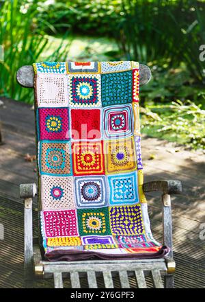 Vintage multi colored blanket, make from crochet granny squares with different motifs, lies on a wooden garden league outdoor. Copy space. Stock Photo