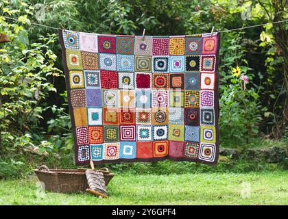 Vintage colorful blanket, make from crochet granny squares with different motifs, hangs on the string in the summer cottage garden. Stock Photo