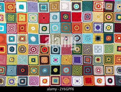 Top view of handmade multi colored plaid make from crochet granny squares with different motifs. Beautiful handicraft product for warm in wintertime. Stock Photo