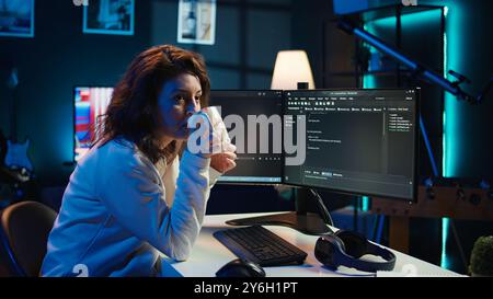Portrait of smiling IT specialist drinking coffee while looking for company security vulnerabilities and preventing malware infections. Programmer enjoying hot beverage while writing code, camera B Stock Photo