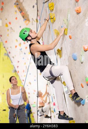 Determined young man in safety helmet doing his best at climbing artificial wall Stock Photo