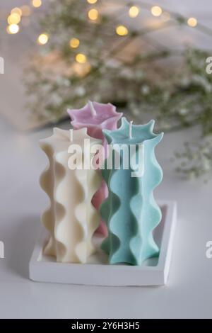 Three soy candles on a table with a book, flowers and lights in background. Home decor. Cozy interior. Stock Photo