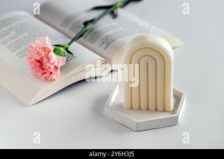 White soy candle on a table with a book and flowers. Home decor. Cozy interior. Stock Photo