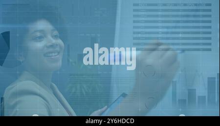 Image of diagrams and data processing over biracial businesswoman taking notes Stock Photo
