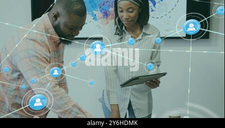 Image of network of connections with people icons over diverse business people in office Stock Photo