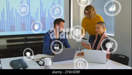 Image of icons over diverse collleagues working in office Stock Photo