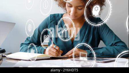 Image of icons over diverse collleagues working in office Stock Photo