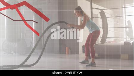 Using battle ropes, woman exercising over declining red graph image Stock Photo