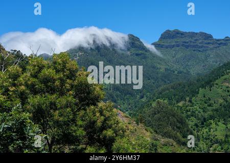 Clouds held on the north side of Madeira's mountainous spine start to fall over the crest and blanket the forested slopes Stock Photo
