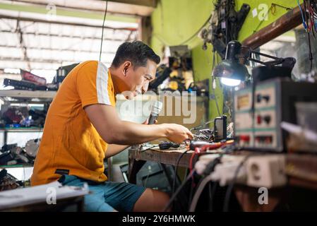 Asian male technician fixes broken cable in electronics repair room Stock Photo