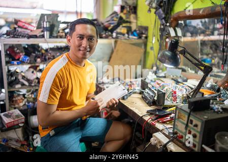 electronics repairman smiles while writing a repair list in the repair room Stock Photo