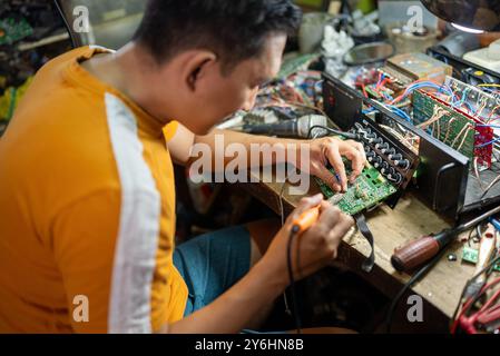 Asian repairman uses electric soldering iron to repair electronic circuit on workbench Stock Photo