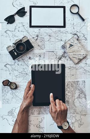 Planning journey. Close up top view of man using digital tablet with sunglasses, photo camera, compass, magnifying glass and passport lying on map aro Stock Photo