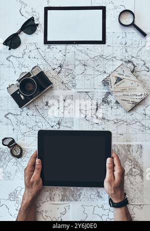 Ready to travel. Close up top view of man using digital tablet with sunglasses, photo camera, compass, magnifying glass and passport lying on map arou Stock Photo