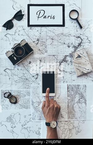 Planning new destination. Close up top view of man using smart phone in front of the map Stock Photo