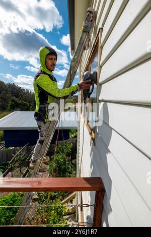Painter on ladder doing surface preparation on a timber weatherboard home in Hobart, Tasmania Stock Photo
