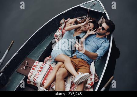 Young and playful couple. Top view of beautiful young couple taking selfie using smart phone while lying in the boat Stock Photo