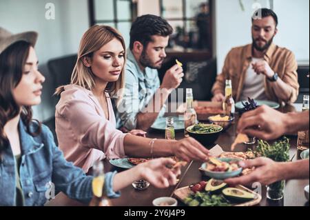 Just hungry. Group of young people in casual clothing eating while having a dinner party indoors Stock Photo