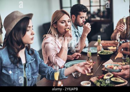 Leave all the worries behind. Group of young people in casual clothing eating while having a dinner party indoors Stock Photo