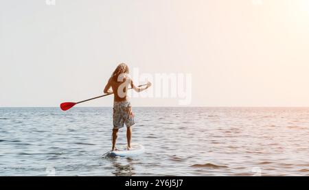 Man Paddleboarding Ocean - Young man enjoys paddleboarding on a calm ocean during a summer day. Stock Photo