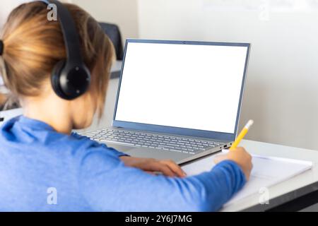 In school, boy wearing headphones writing in notebook while using laptop, copy space Stock Photo