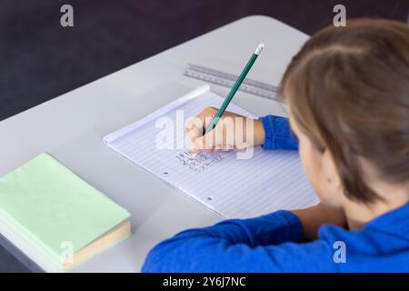 Writing math equations in notebook, boy focusing on schoolwork at desk Stock Photo