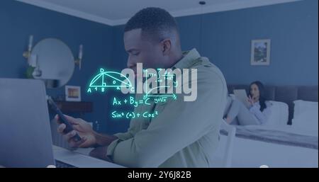 Image of equations over african american man using laptop and smartphone in bedroom Stock Photo