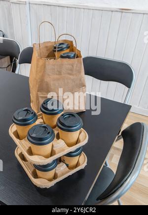 A table with a stack of coffee cups and a brown paper bag. The table is black and is in an office with white walls. Stock Photo