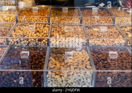 Various types of nuts are arranged neatly in transparent bins at a marketplace. Stock Photo