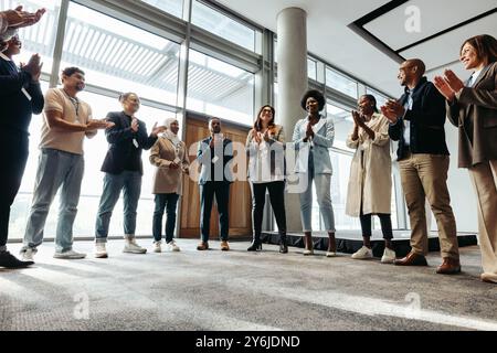 Diverse group of business professionals clapping and celebrating in a modern office during a motivational team building session. Stock Photo