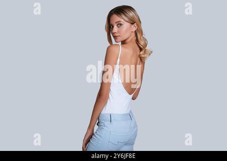 Simply stunning. Attractive young woman looking at camera over shoulder while standing against grey background Stock Photo