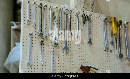 Various tools: file, screwdriver, hammer, pliers, garden tools are displayed on wooden shelf inside rustic garage or manufactory, workshop studio in a Stock Photo